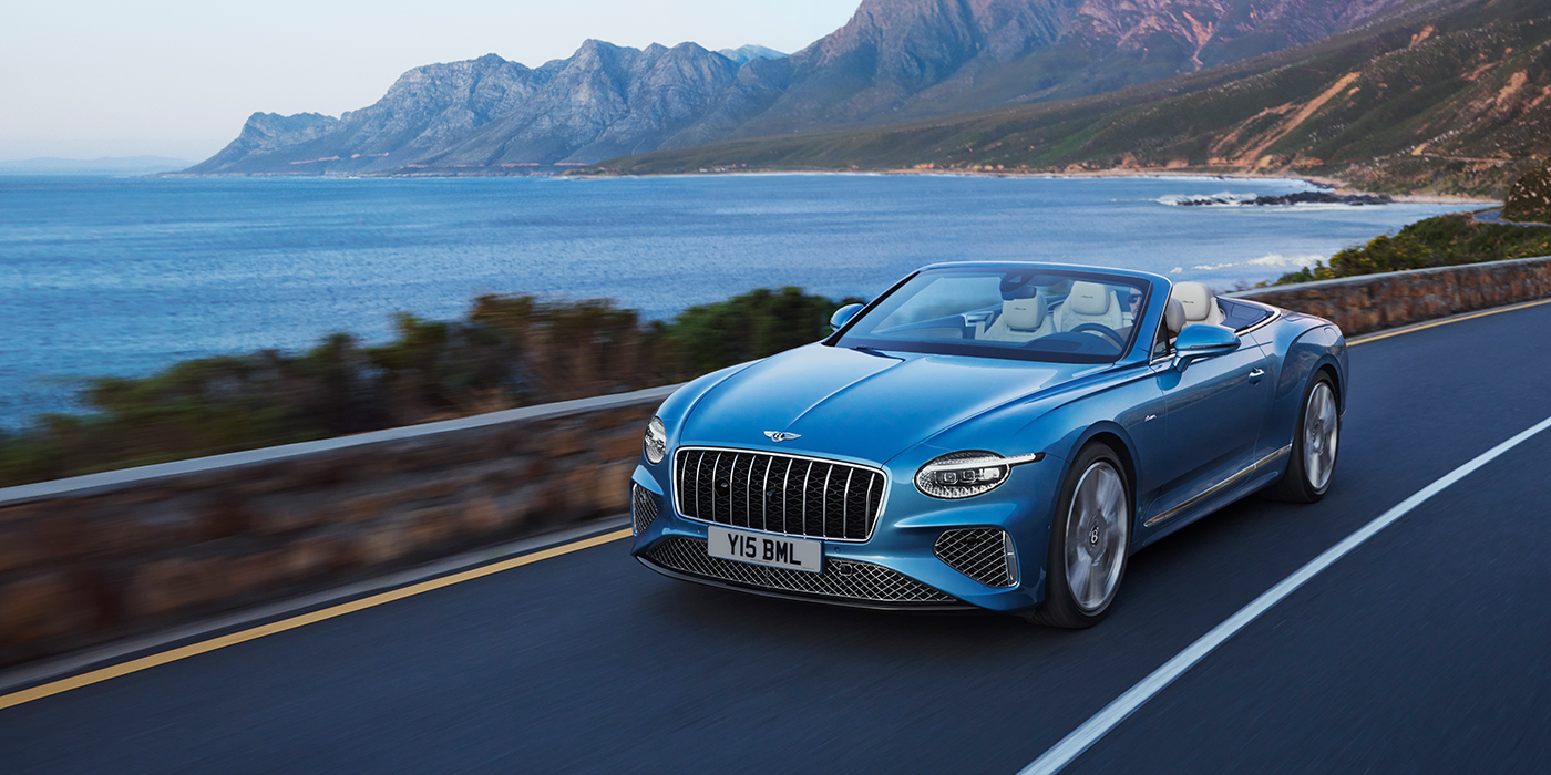 Bentley Roma New Bentley Continental GTC Azure convertible in Light Windsor blue paint with 22 inch Azure wheels and chrome grill, driving dynamically by the sea