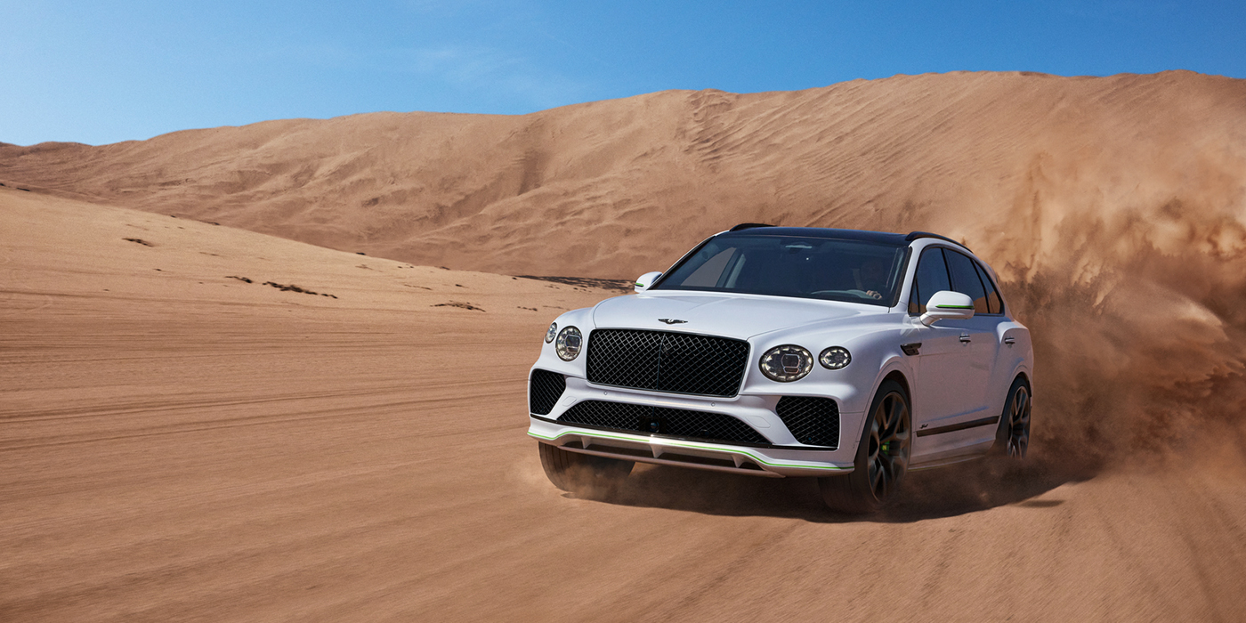Bentley Roma Bentley Bentayga Speed SUV front three quarter in Snow Quarts Pearlescent by Mulliner white paint driving dynamically through the desert