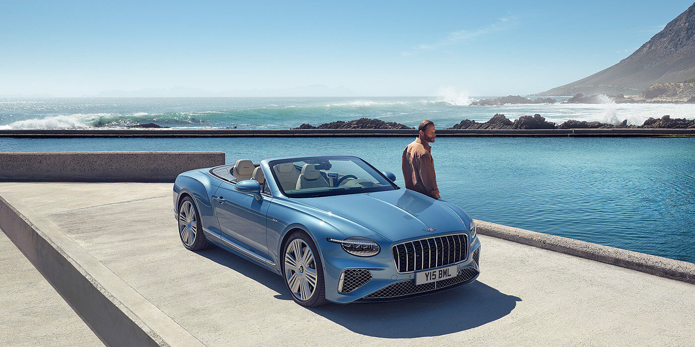 Bentley Roma New Bentley Continental GTC Azure convertible front view in Light Windsor blue paint with 22 inch ten spoke wheels parked by the sea in the sunshine