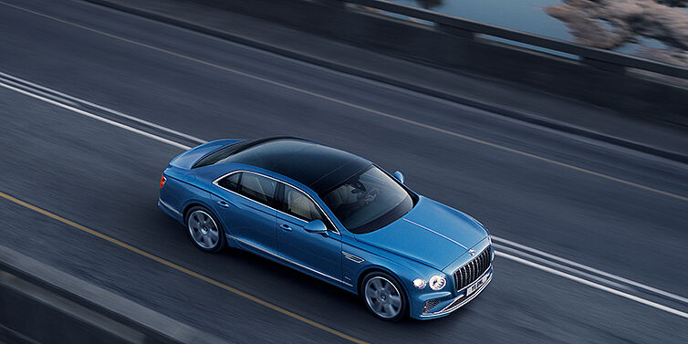 Bentley Roma New Bentley Flying Spur Azure sedan in Light windsor blue paint by Mulliner, with 22 inch Azure wheels seen from overhead driving dynamically on a country road
